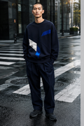 Male model wearing the navy Crosswalk Core oversized crewneck on a rain-dark crosswalk