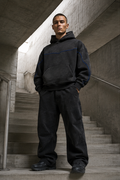Male model wearing the washed-black District Zero oversized hoodie on concrete stairs